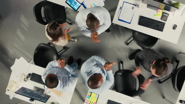 Top down view zoom out of professional coworkers engaged in report sharing and data visualization. Multiethnic team uses forecasting and documentation to strengthen business strategy. Camera A.