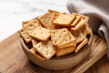 Wooden bowl with tasty crackers on white background, closeup