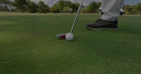 Lining up golfer in golf shoes placing putter behind white golf ball on putting green