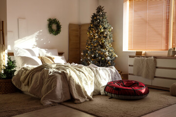 Inflatable sled, chest of drawers, bed and Christmas tree in interior of light bedroom