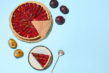Tasty plum pie with fresh fruits and spoon on blue background