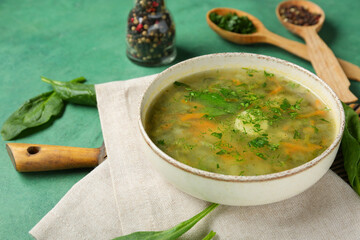 Bowl of tasty green borscht with peppercorns, greens and spinach leaves on green grunge background