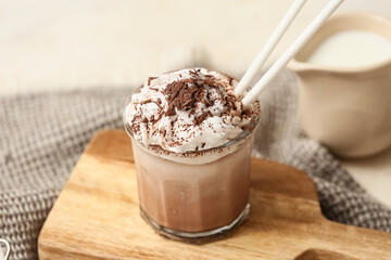 Glass of cold cocoa drink with whipped cream and jug of fresh milk on white background, closeup