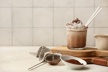 Glass of cold cocoa drink with whipped cream and powder on white table