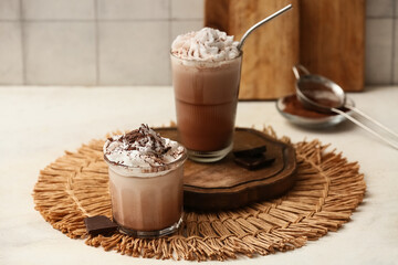 Glasses of cold cocoa drink with whipped cream and chocolate on white table
