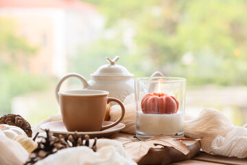 Cup of tea and burning candle on table near window in kitchen, closeup