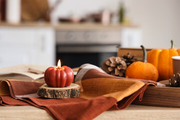 Burning candle in shape of pumpkin on table in kitchen, closeup