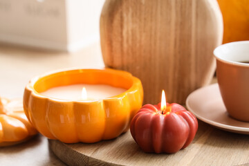 Burning candles in shape of pumpkin on table in living room, closeup