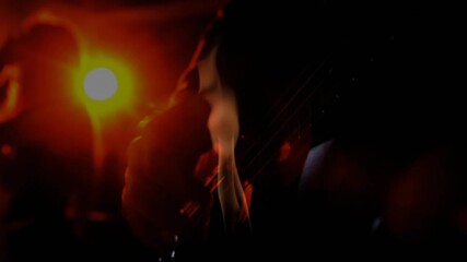 Orange spotlight shining on rising smoke warming guitar strings while musician strumming into mic