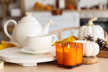 Teapot, cup of tea and burning candle on table in kitchen, closeup