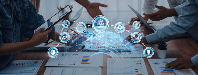 Business professionals engage in a collaborative meeting, utilizing data-driven strategies supported by digital graphics and charts in a modern office setting. Trope