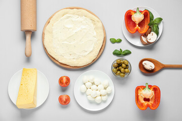 Pizza dough with tasty sauce, rolling pin and ingredients on grey background