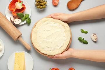 Female hands with pizza dough, tasty sauce and ingredients on grey background