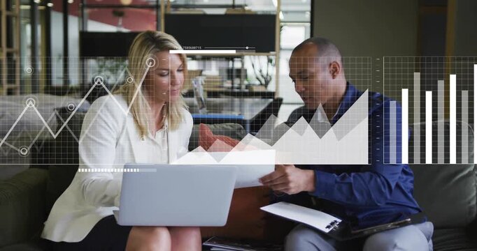 Team in lounge examining report and reviewing laptop data while animated business charts evolving