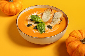 Bowl of delicious pumpkin cream soup with seeds, croutons and basil on orange background