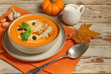 Bowl of delicious pumpkin cream soup with seeds, croutons, basil and garlic on wooden background