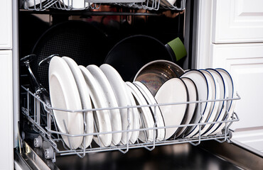 Clean white plates and cookware in built-in dishwasher on modern kitchen setting with efficient design