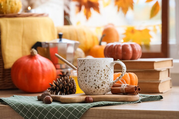 Cup of pumpkin latte with books and autumn decor on table near window at home, closeup