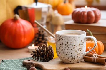 Cup of pumpkin latte with books and autumn decor on table in living room, closeup