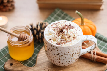 Cup of pumpkin latte with honey and autumn decor on table in living room at home, closeup