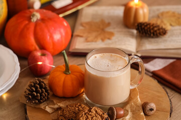 Cup of pumpkin latte with cookies, book and autumn decor on table at home