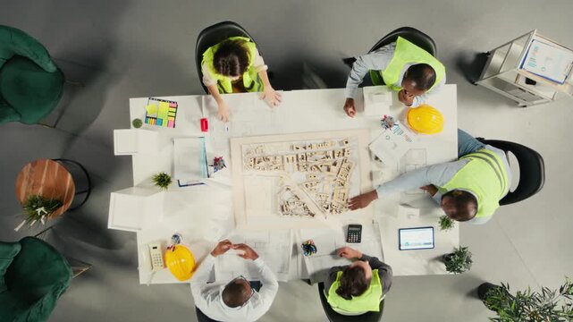 Top down view zoom in of architects working on real estate investment plan. Business team analyzes property data, housing blueprints and trends to optimize land acquisition and projects. Camera A.