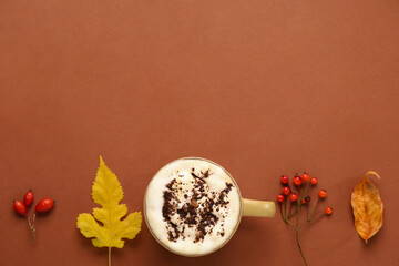 Composition with mug of coffee, autumn leaves and berries on brown background