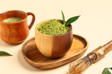 Cup of fresh matcha tea, chasen and bowl with powder on beige background