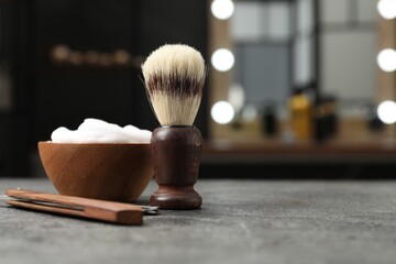 Shaving brush, foam and straight razor on grey textured table in barbershop, closeup. Space for text