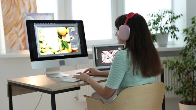 Professional retoucher putting on headphones and editing photo on computer at table in office