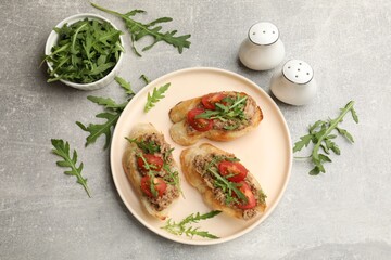 Delicious bruschettas with tuna, tomatoes and arugula on grey table, flat lay