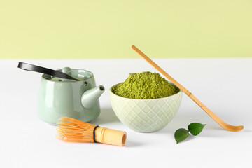 Bowl with powdered matcha tea, chashaku, chasen and teapot on color background