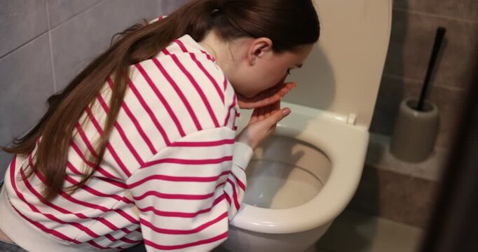 Woman suffering from nausea over toilet bowl in bathroom, camera moving in