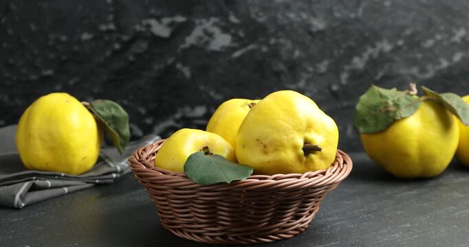 Woman taking ripe quince from wicker basket at black table, closeup