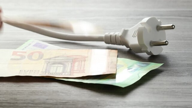 Woman putting euro banknotes near electrical plug at wooden table, closeup