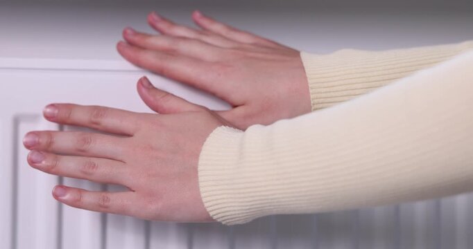 Woman warming her hands near radiator indoors, closeup