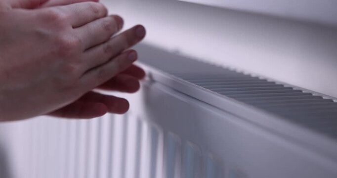 Woman warming her hands near radiator indoors, closeup