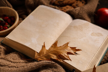 Book with sweater and autumn decorations on brown wooden background