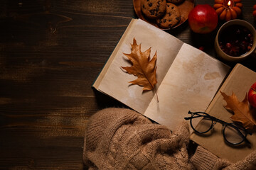 Books with cup of tea, cookies, sweater and autumn decorations on brown wooden background