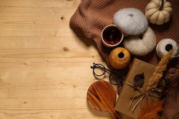 Book with cup of tea, knitting yarn, sweater and autumn decorations on brown wooden background