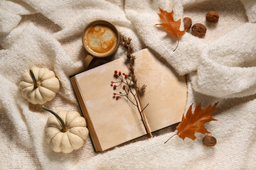 Book with cup of coffee, pumpkins and autumn decorations on warm white plaid background