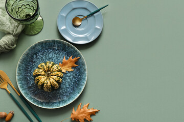 Beautiful table setting with pumpkin, acorns and autumn leaves on green background