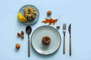 Beautiful table setting with pumpkin, pine cones and dandelion flowers on blue background