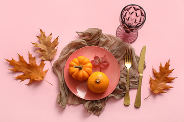 Beautiful table setting with pumpkins and autumn leaves on pink background