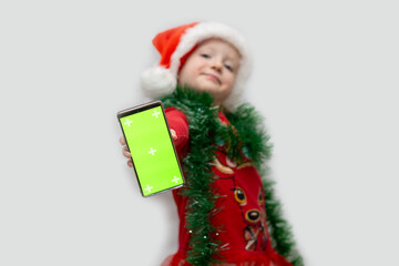 Child in Christmas outfit holding smartphone with a bright green screen during festive season