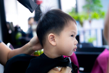 Side profile of young boy receiving the finishing touches on his new haircut, with a stylist using...