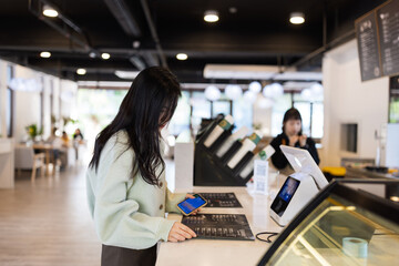 Young woman browsing a menu at a modern cafe counter with smartphone in hand