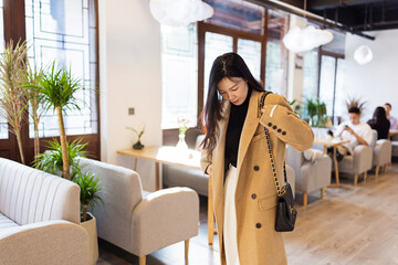 Young woman adjusting her coat while standing in a modern cafe
