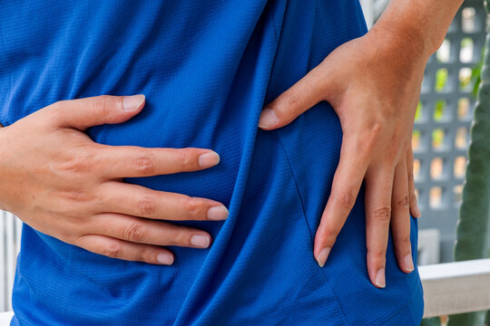 Man clutching lower left abdomen, showing signs of localized pain or digestive discomfort. Medical concept for abdominal cramps or gastrointestinal issues.