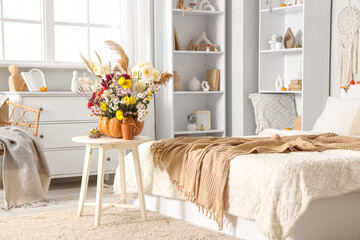 Mug of tea and pumpkin with autumn bouquet on table near bed in interior of bedroom